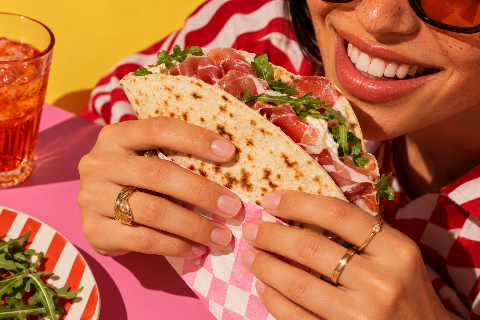 Ragazza che morde una piadina con prosciutto crudo e rucola su un tavolo rosa